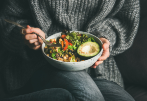 An image of a woman eating salad avocado half beans grains and vegetables out of a bowl