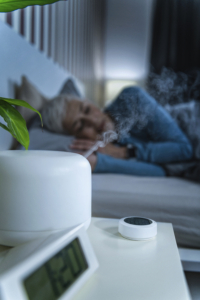 An image of a humidifier blowing steam toward a woman sleeping in bed