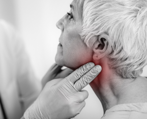 An image of a doctor feeling a woman's reddened neck for throat cancer.