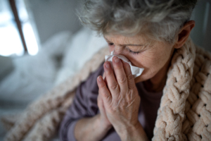 An image of a senior woman with the common cold blowing her nose